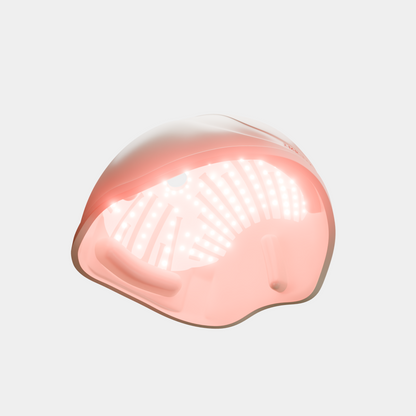 A red light therapy helmet shown on a clean white background, illuminated with a soft pink glow from the internal LED lights.